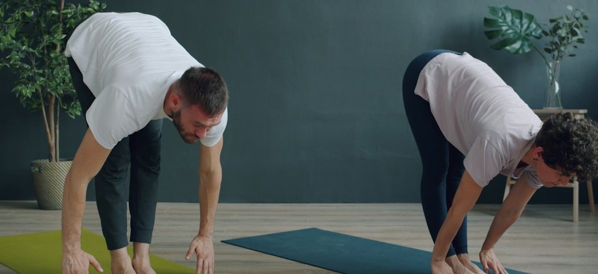 Tilt-up slow motion of man and woman young couple doing yoga in cozy studio bending body then raising arms standing on mats. Youth, healthy lifestyle and people concept.