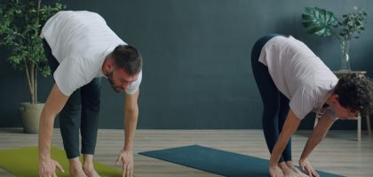 Tilt-up slow motion of man and woman young couple doing yoga in cozy studio bending body then raising arms standing on mats. Youth, healthy lifestyle and people concept.