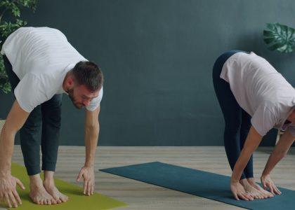 Tilt-up slow motion of man and woman young couple doing yoga in cozy studio bending body then raising arms standing on mats. Youth, healthy lifestyle and people concept.